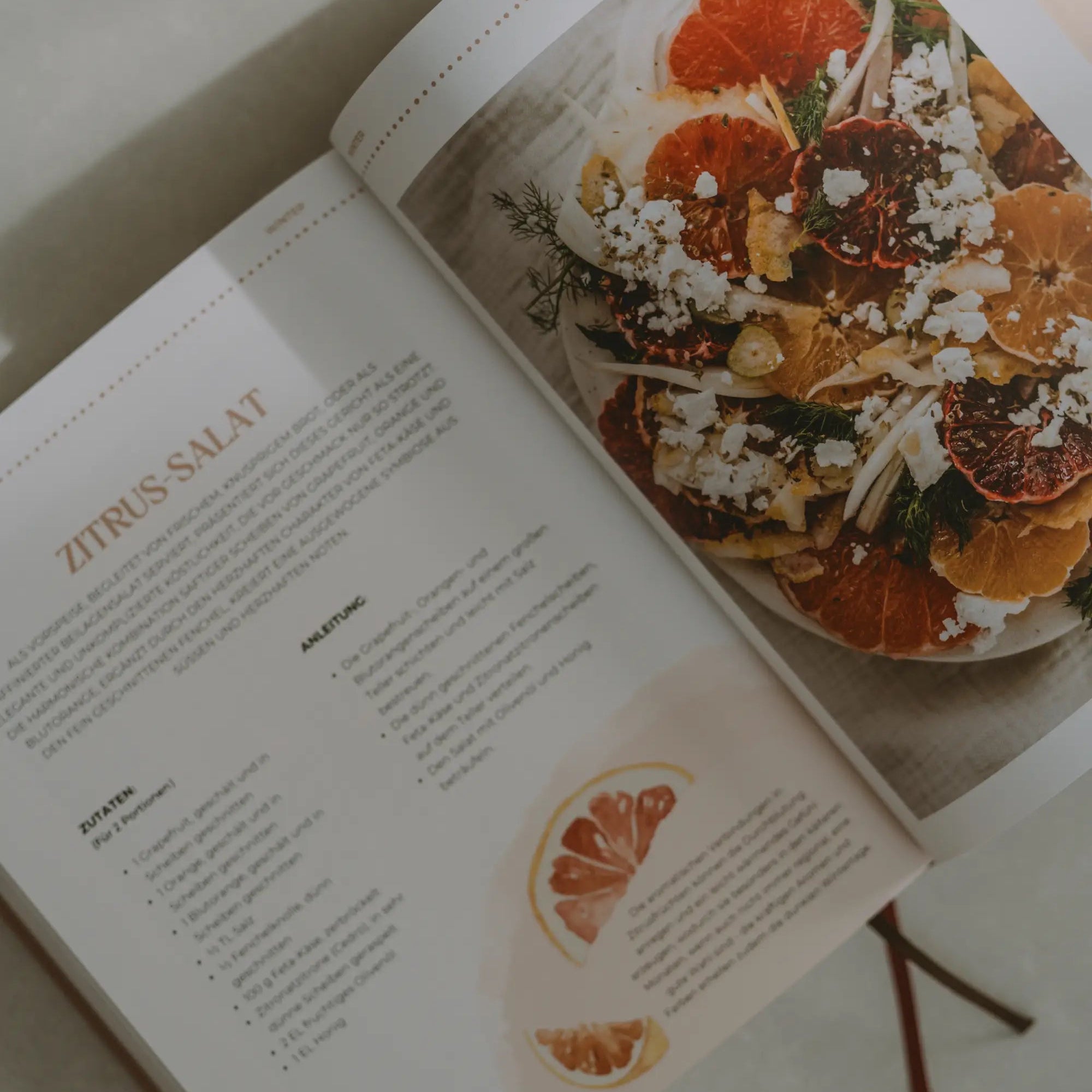 Aufgeschlagenes Kochbuch auf der Seite mit einem Rezept für Zitrus-Salat.